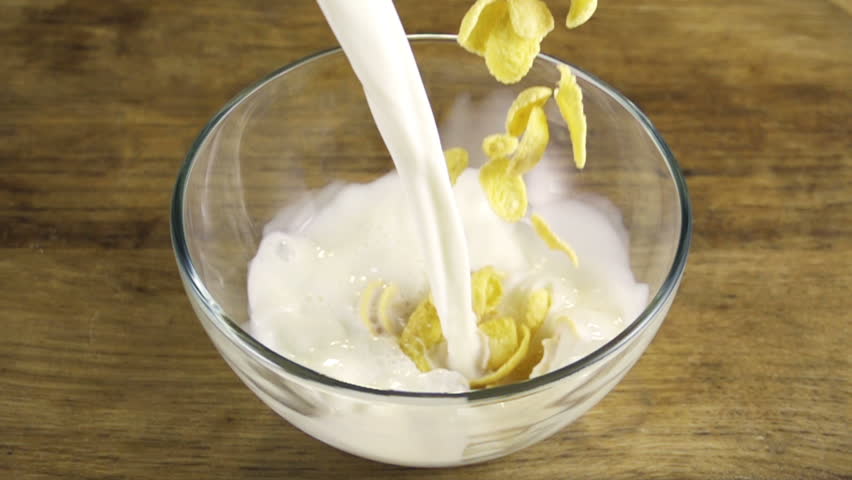 Corn flakes with milk pouring in bowl
