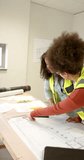 Vertical video of casual diverse female architects looking at plans, slow motion, copy space. Architecture, casual business, work, office, meeting and teamwork concept, unaltered.