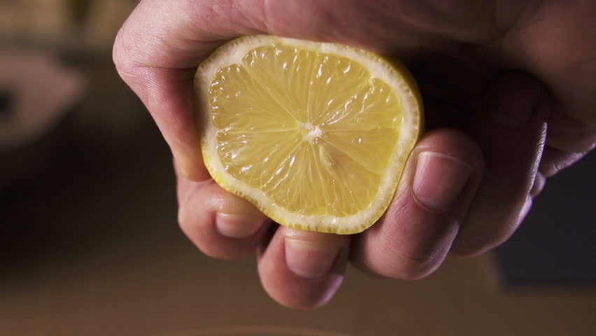 hand squeezing lemon on dark background