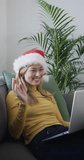 Vertical video of biracial woman wearing santa hat using laptop for video call, slow motion. Communication, celebration, christmas, lifestyle and domestic life, unaltered.