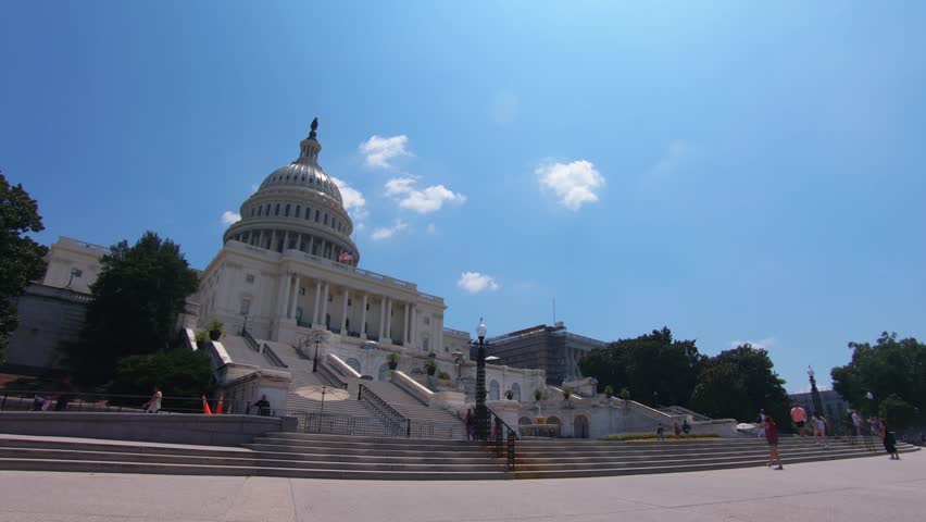 Amazing shot of the US Capitol building and people walking in front of it on a beautiful summer sunny day. The landmark is located in the Capitol Hill, National Mall