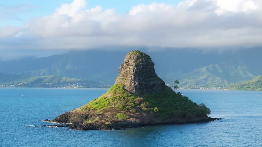 Epic aerial around Mokolii volcanic island with green mountains on motion background. Chinese man island aerial at sunrise. Cinematic cloud on Kualoa. Oahu island tourism. Scenic nature landscape