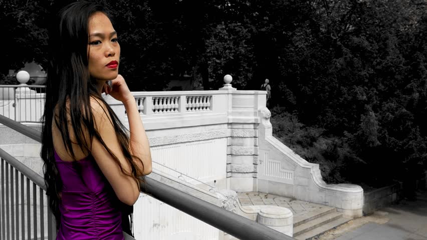 Asian woman in purple dress looking contemplative and observes something. Closeup, slowmotion. Vienna, Austria.