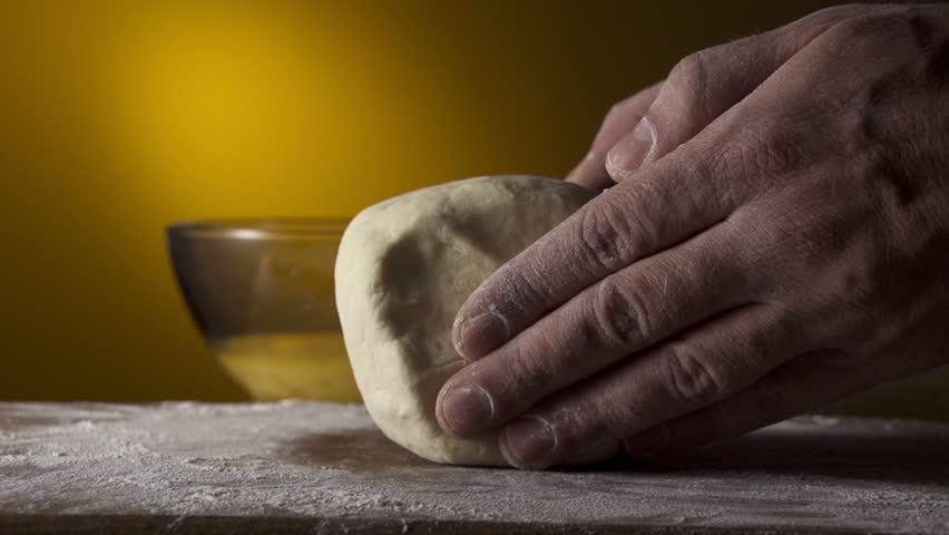 Hands of the baker knead a piece dough in a flour, slow motion