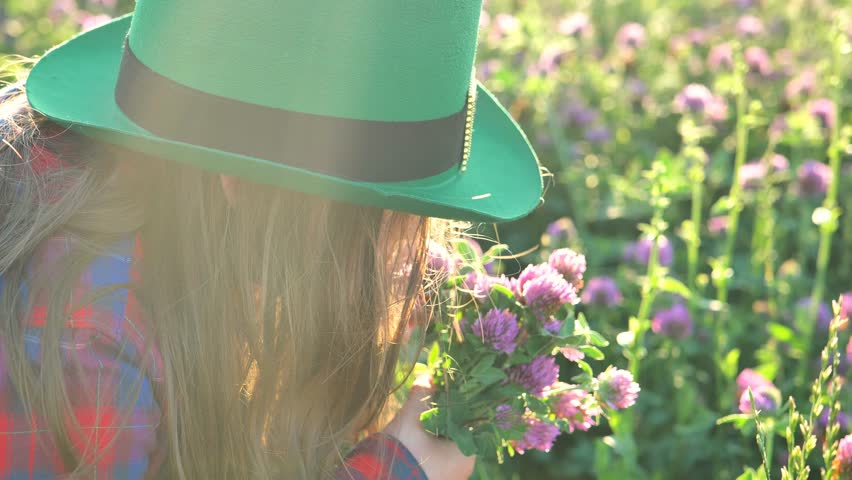 St.Patricks Day.Girl in a leprechaun hat with a bouquet of clovers in a sunny clover field.Saint Patrick festive. Good luck symbol. Irish traditional spring holiday symbol. 4k footage