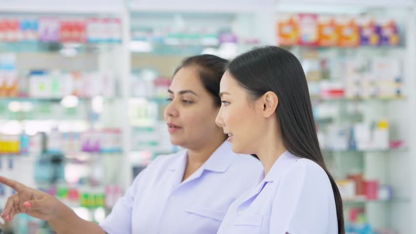4K Medical pharmacy and health care business concept. Asian woman pharmacist colleague working together on computer checking medical product, drugs, medicine and supplements in modern drugstore.