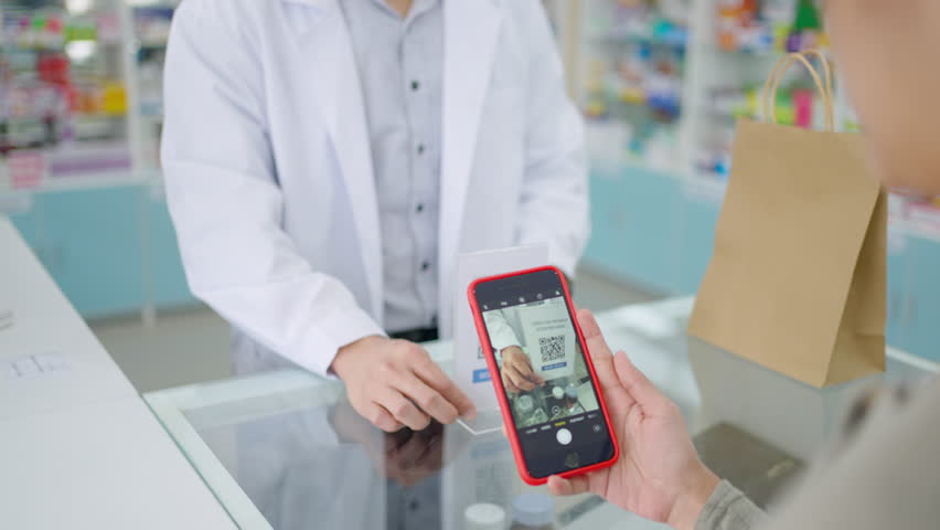 Medical pharmacy and contactless payment concept. Asian woman patient customer using mobile phone scan QR code on counter making online baking payment buying medicine and supplements in drugstore.