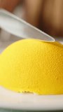A woman slowly cuts a lemon mousse dessert in half, close-up. Vertical video.
