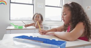 Video of biracial girls sitting at school desks and learning. primary school education, knowledge and learning concept.