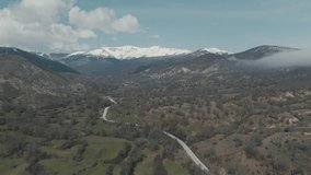 A drone shot of forest mountains with snow, warm weather, little village, flying above a foggy hill, 4K video, European winter nature, scenic white clouds, beautiful landscape