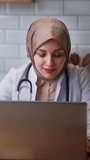 Vertical video. Young female doctor in headscarf wears white coat talking to patient using virtual chat computer app. Remote healthcare services concept