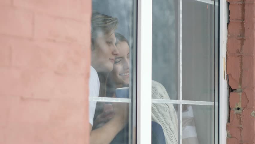 Brick wall and a big window. Two loving people sitting at the window and looking outside.