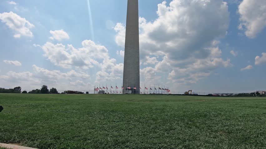 Tilt shot of the famous Washington monument with American waving flags around. This monument is an obelisk shaped building within the National Mall in Washington, DC