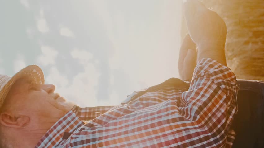Mature man exploring ripe wheat field. Male in checkered shirt and straw hat. Senior farmer at wheat plot. Male agricultural businessman at sunlight. Farmer holding tablet. Vertical shot.