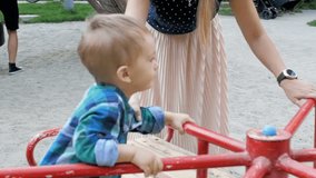 Slow motion video of young mother riding her toddler boy on colorful carousel at park