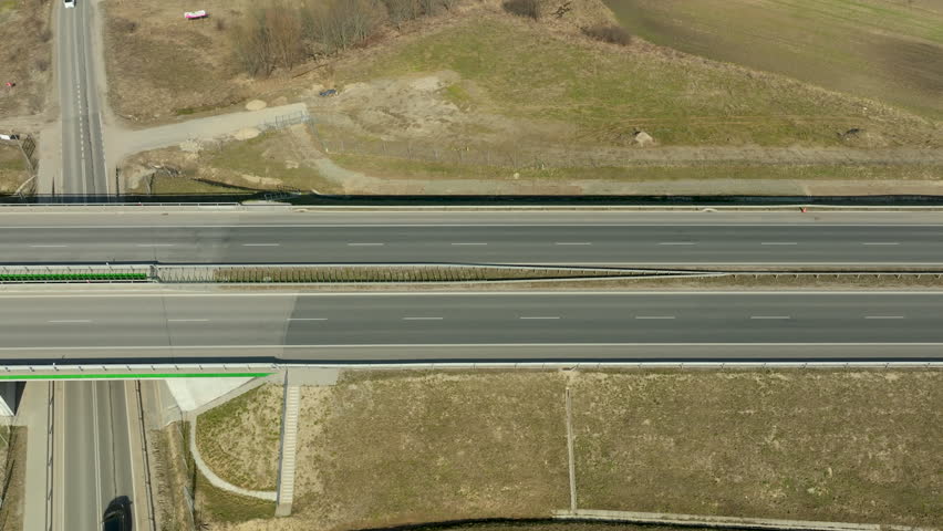 Aerial view of a highway with two cars driving in opposite directions, surrounded by open fields and scattered trees.