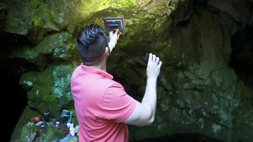Holding up a recorder, a man is recording some environmental ambient sounds in front of a cave known as the location of the tomb of the Egyptian goddess Bastet at Strandzha Mountain in Bulgaria.