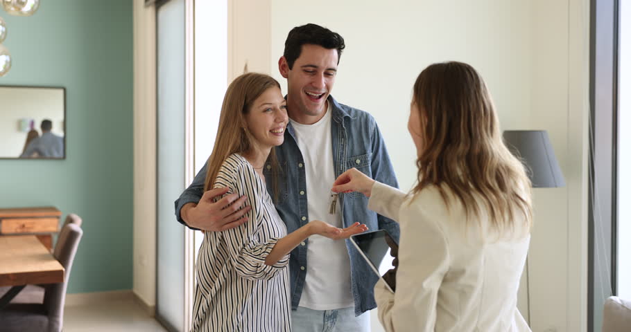 Happy young spouses get keys from their new house at meeting with realtor. Rea-estate agent shake hands to Hispanic couple, gives them keys from apartment after signing contract. Bank loan, relocation