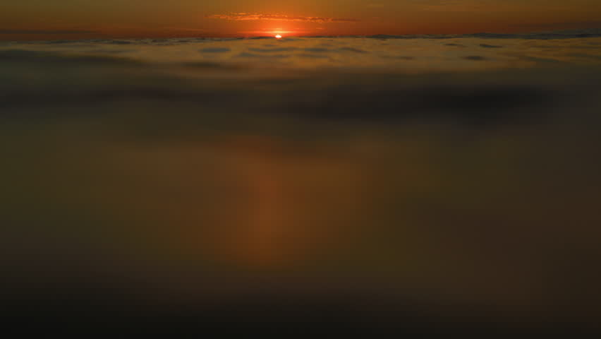 Red setting sun ball drops low on horizon as ocean water waves rise and fall with tide