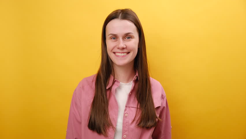 Portrait of emotional young caucasian woman in pink shirt, showing tasty gesture, kisses fingers and says bellissimo, looking at camera, isolated on yellow studio background. Gourmet culinary concept