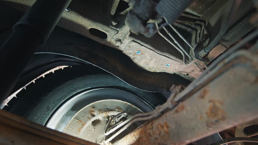 Undercarriage perspective highlighting a tire and suspension system, detailing the wear and workmanship in a car service setting. Royalty-Free Stock Footage #3465422083