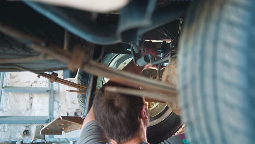 View of a focused mechanic working on a car's undercarriage and suspension in a bright workshop setting Royalty-Free Stock Footage #3465422171