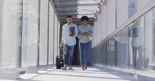 Video of diverse businessman and businesswoman walking with suitcase and talking. business professionals and working in office concept.