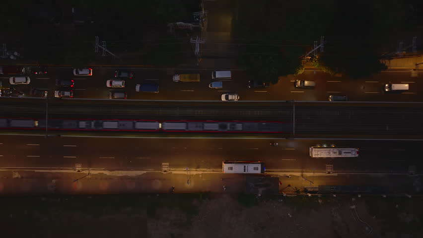 Birds eye shot of traffic in evening city. Cars stopping on multilane road at traffic lights and commuter train passing by them. Manila, Philippines