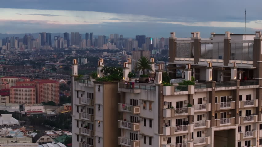 People enjoying view of rooftop terrace of high rise building. Aerial ascending shot of Torre de Manila and city in background. Manila, Philippines