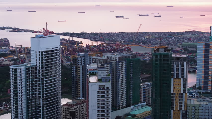 Aerial view of high rise buildings in urban borough and seaport with huge cranes in background. Manila, Philippines