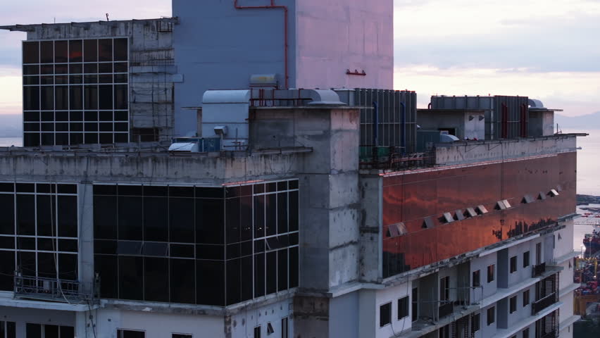 Fly around top of tall residential building in city. Revealing Sea coast and port at twilight. Manila, Philippines
