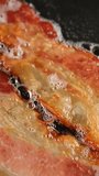 Frying bacon slices in hot pan, slider shot. Vertical video