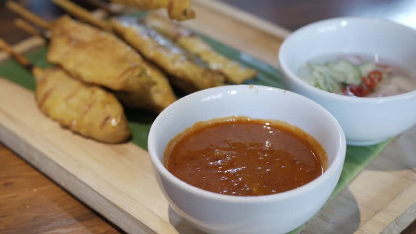hand grabing satay skewer bbq chicken on a plate in traditional singaporean or malaysian style in traditional cruisine dipping into the sauce for appetizer before meal or snack Royalty-Free Stock Footage #3465613351
