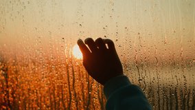 Silhouette of finger trying to touch evening sun behind wet window closeup. Hand touches glass with leaking water pattern. Dreaming at dusk - Powered by Shutterstock - Get 15% off with code: PIKWIZARD15