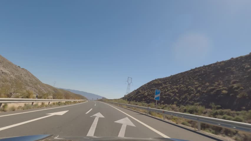 First person view, FPV, from dashcam of car driving mountain road from Calar Alto Observatory to Tabernas Desert in Almeria, Andalusia, Spain, Europe. Road trip in POV, with bright, sunny, clear sky