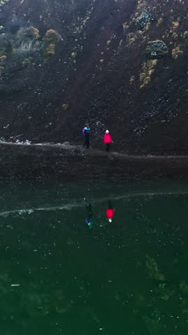A young scientist couple walking on volcanic hills exploring eruption dangers in Iceland, vertical composition