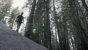 Fearless handsome well built tourist in summer hiking outfit with hiking gear moving down a huge smooth stone on a cloudy day in Yosemite national park. High quality 4k footage