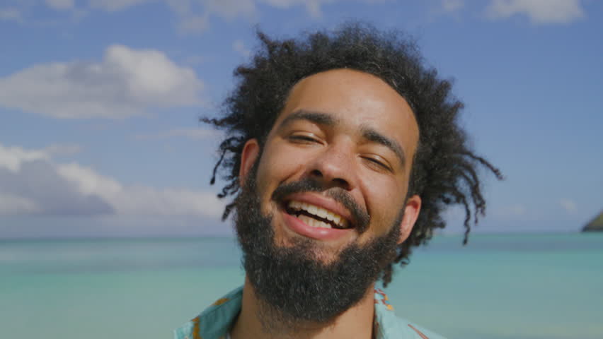 Close up of excited male tourist with dark curly hair showing his charming smile, shaking head, standing over fascinating view of blue ocean and skies. High quality 4k footage Royalty-Free Stock Footage #3465978499
