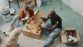 Young Caucasian woman sitting on floor with African American husband, eating pizza and giving piece to dog when taking break during DIY home renovation. High angle view - Powered by Shutterstock - Get 15% off with code: PIKWIZARD15