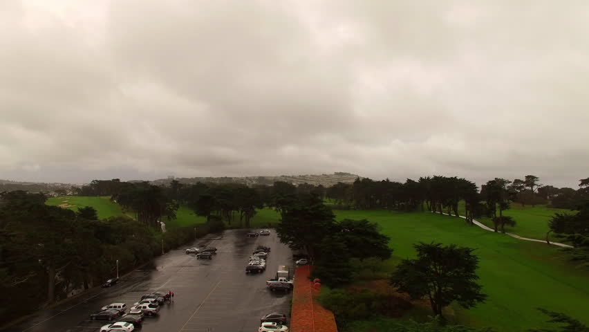 Aerial: Drone Backward Shot Of Cars Parked In Parking Lot On Green Hill Under Cloudy Sky - San Francisco, California