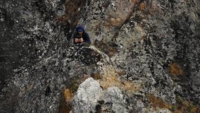 Man sits on rocks in the mountains of Georgia controlling a drone with remote control in his hand to capture stunning aerial footage. Male caucasian tourist travels to Birtvisi and explores rocks
