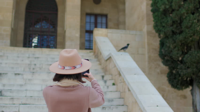 young woman takes pictures of beautiful views of the city on her phone while traveling through the old city. Young attractive smiling tourist girl exploring a new city.