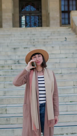 vertical shot. Happy young girl in a hat speaks on the phone. girl walking
in the city. Europe travel concept.