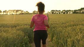 4K video clip of beautiful healthy mixed race African American girl teenager female young woman runner running on path through field of barley or wheat crops at sunset