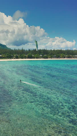 Aerial view kitesurfer speeding with kite in clear crystal water from drone. An athlete rides a kite in the Indian Ocean on the island of Mauritius. Live reef near island. Conquest of the sea