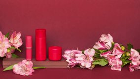 Video of natural anti-aging cosmetics with floral extract in red packaging on podium and fresh pink flowers on brown background.  The concept of the presentation of new types of spring cosmetics