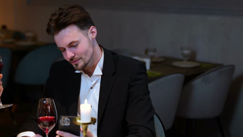 Happy young man holding smartphone while making selfie with her girlfriend during date in the restaurant. Lifestyle, love, relationships concept. Slow motion