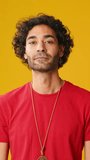 Vertical video, Surprised man with curly hair, dressed in red T-shirt, looks to side to show copy-space isolated on yellow background in studio
