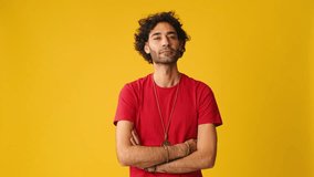 An attractive man with curly hair, dressed in red T-shirt, listens and agrees while looking at camera isolated on yellow background in studio