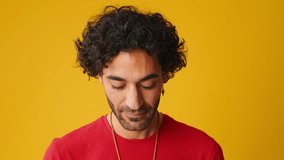 Close-up, man with curly hair, dressed in red T-shirt, raises his head and looks at camera isolated on yellow background in studio